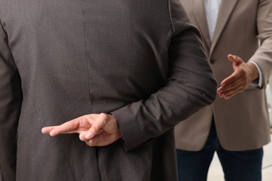 Employee crossing fingers behind his back while meeting with boss indoors, closeup