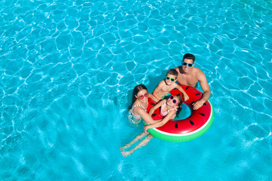 Image of Happy family with inflatable ring in swimming pool, space for text. Summer vacation 
