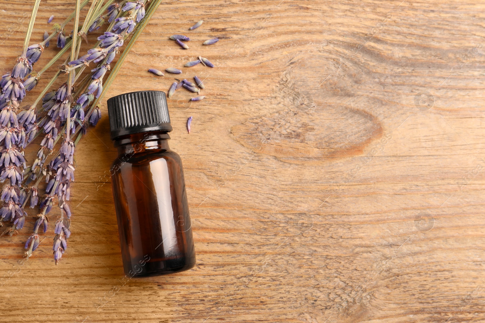 Photo of Bottle of essential oil and lavender flowers on wooden table, flat lay. Space for text