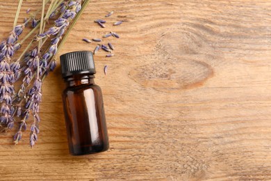 Photo of Bottle of essential oil and lavender flowers on wooden table, flat lay. Space for text