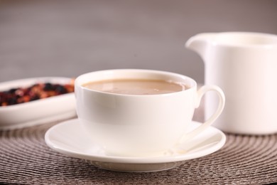 Photo of Cup of aromatic tea with milk and saucer on table, closeup