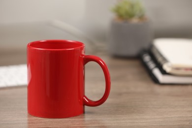 Photo of Red ceramic mug on wooden table at workplace. Space for text