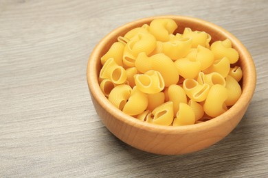 Photo of Raw macaroni pasta in bowl on light grey wooden table, closeup. Space for text