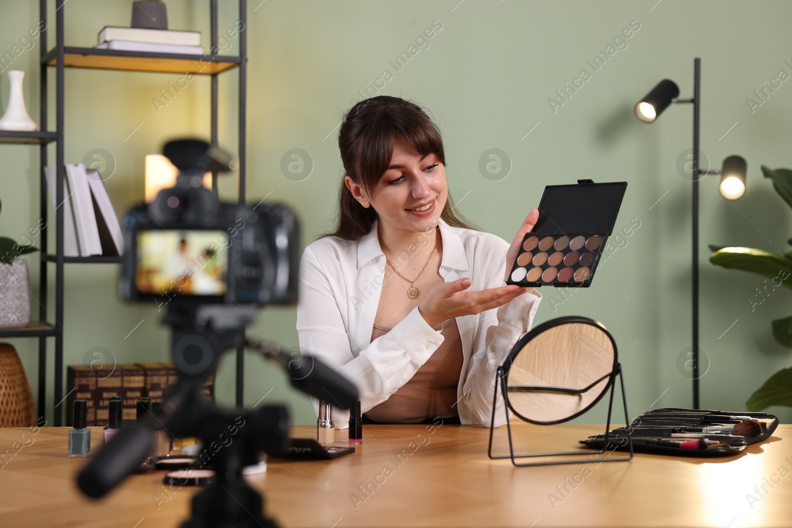 Photo of Smiling beauty blogger recording video while showing eyeshadow palette at home