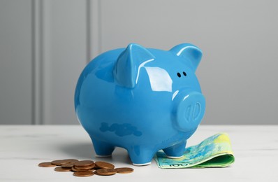 Photo of Ceramic piggy bank, banknotes and coins on white marble table