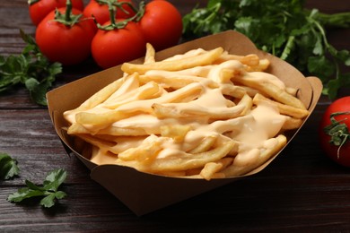 Tasty potato fries, cheese sauce in paper container and products on wooden table, closeup