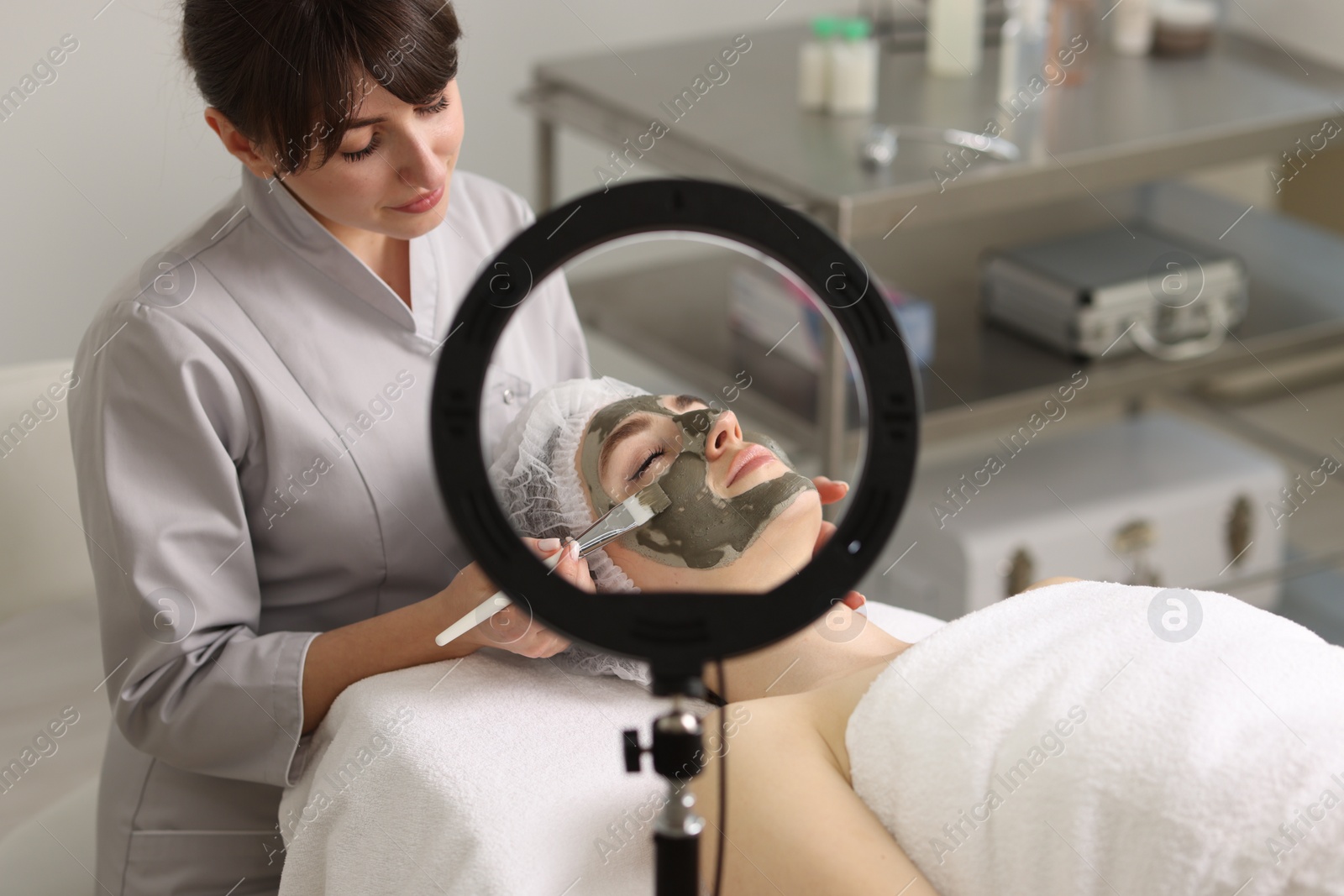 Photo of Cosmetologist applying mask on woman's face in clinic