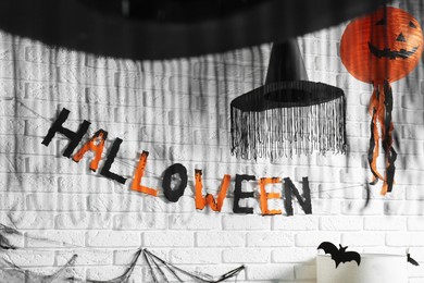 Photo of Word Halloween made of colorful letters and festive decor on brick wall