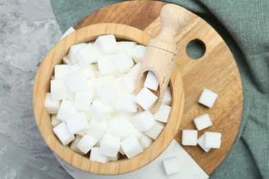 White sugar cubes in wooden bowl and scoop on grey table, top view