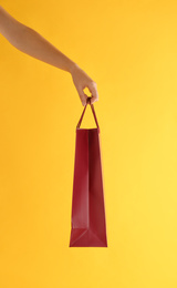 Woman with paper shopping bag on yellow background, closeup