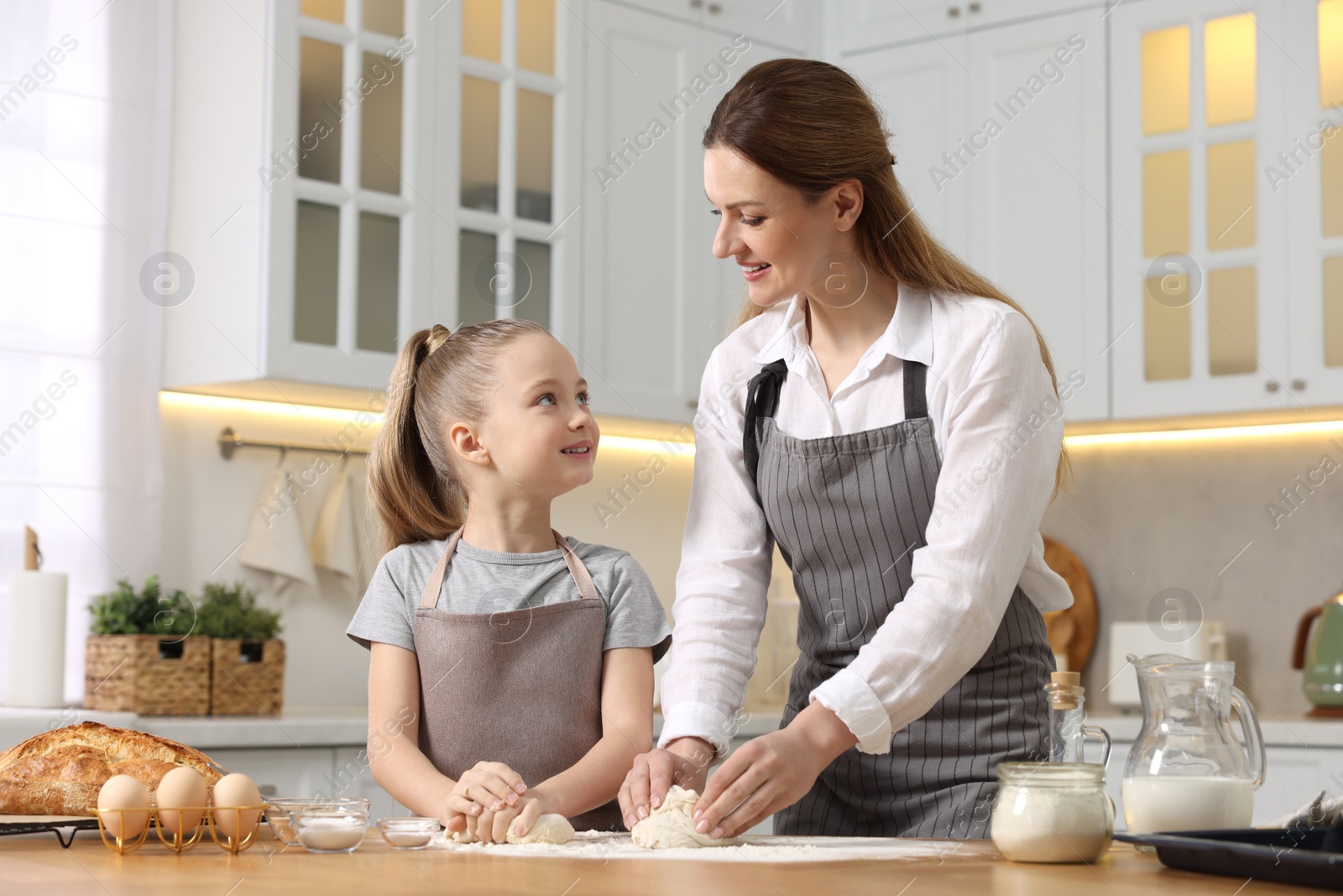 Photo of Making bread. Mother and her daughter kneading dough at wooden table in kitchen