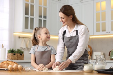 Making bread. Mother and her daughter kneading dough at wooden table in kitchen