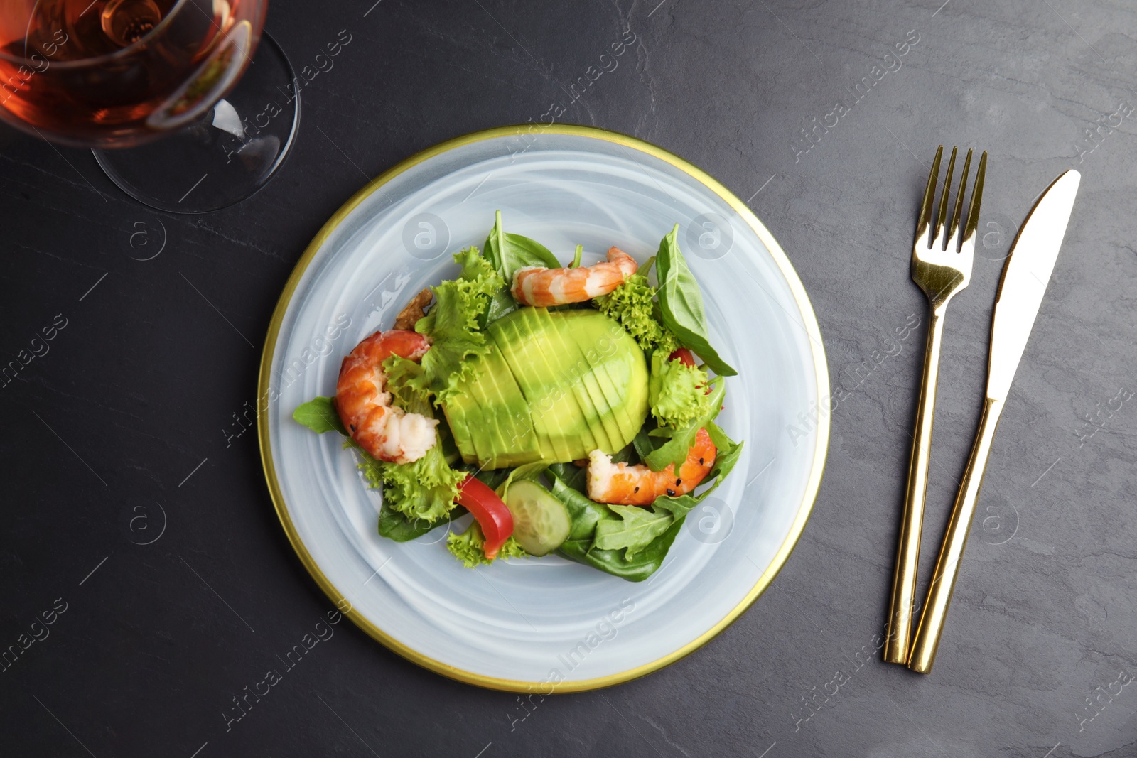 Photo of Delicious avocado salad with shrimps on black table, flat lay