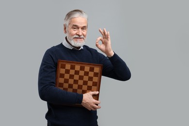 Photo of Man with chessboard showing OK gesture on light gray background. Space for text