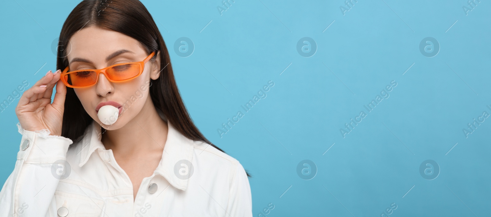 Photo of Beautiful woman in sunglasses blowing bubble gum on light blue background, space for text