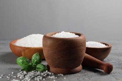 Photo of Pestle and mortar with natural sea salt on grey wooden table