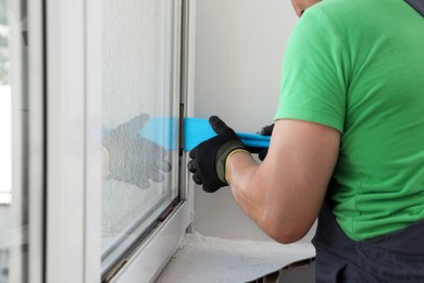 Photo of Worker using spatula for double glazing window installation indoors, closeup