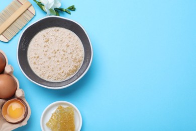 Homemade hair mask in bowl, fresh ingredients and bamboo comb on light blue background, flat lay. Space for text