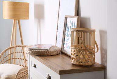 Photo of Stylish wicker holder with candle on chest of drawers indoors