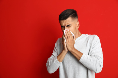 Man sneezing on red background, space for text. Cold symptoms