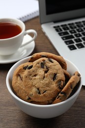 Photo of Chocolate chip cookies, cup of tea and laptop on wooden table