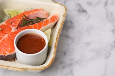 Fresh marinade, fish, lime and rosemary in baking dish on light marble table, closeup. Space for text