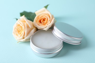 Lip balm and rose flowers on light blue background, closeup
