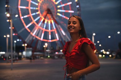 Photo of Beautiful young woman against glowing Ferris wheel in amusement park, space for text