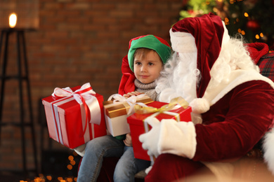 Photo of Santa Claus and little boy with Christmas gifts indoors