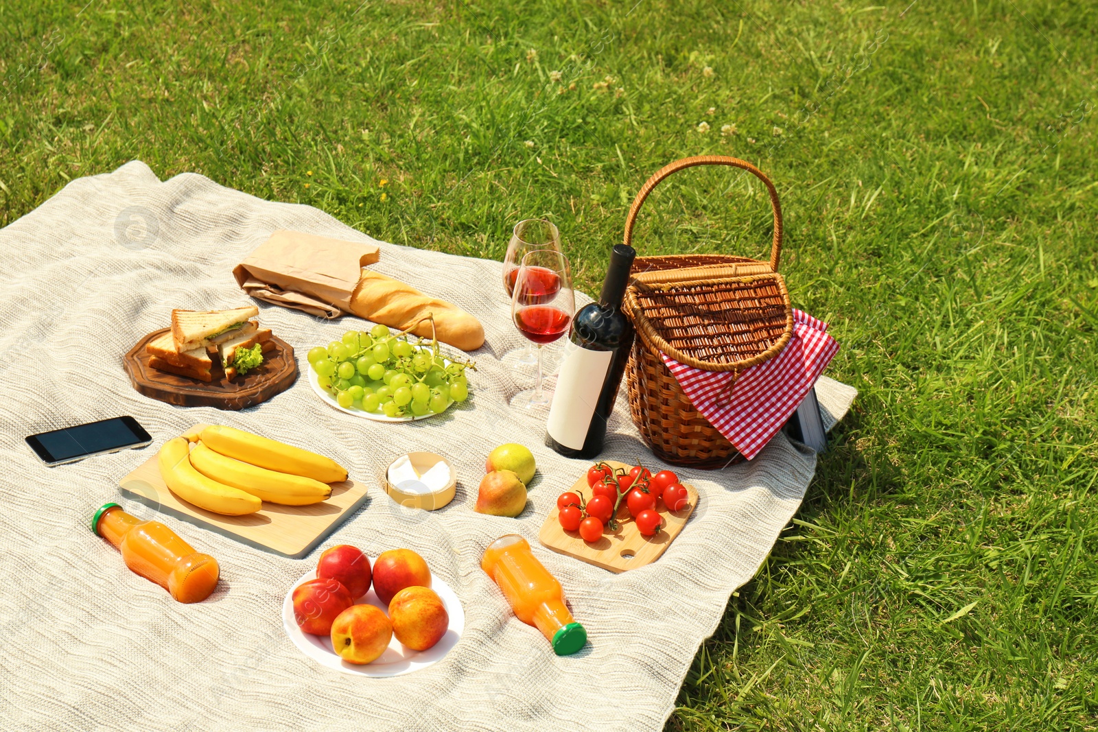 Photo of Wicker basket and food on blanket in park. Summer picnic