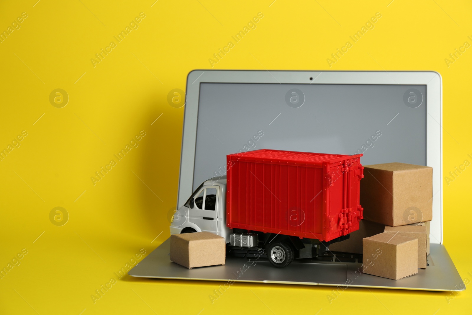 Photo of Laptop, truck model and carton boxes on yellow background. Courier service