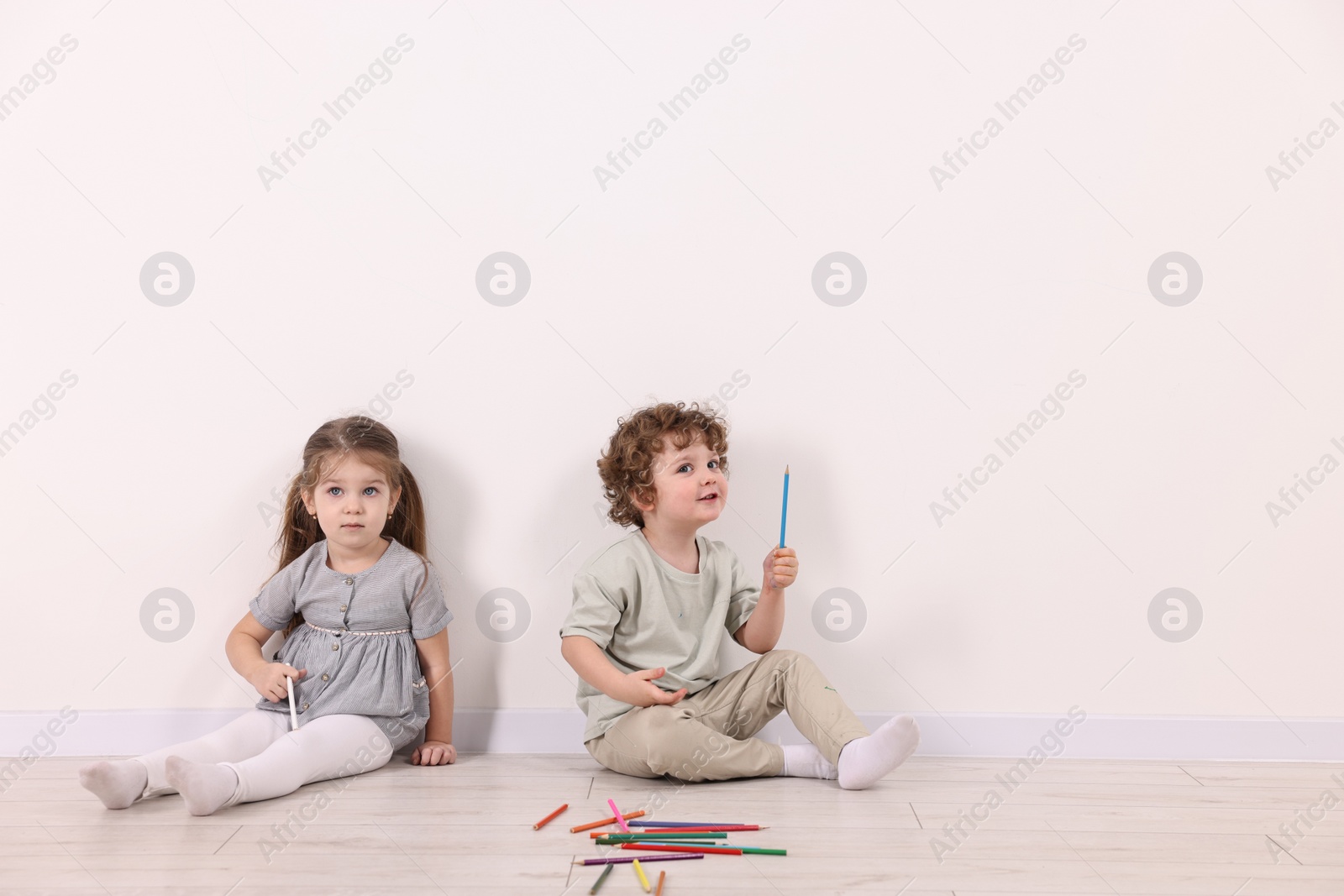 Photo of Cute little children with colorful pencils near white wall indoors. Space for text