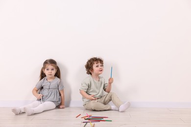Photo of Cute little children with colorful pencils near white wall indoors. Space for text