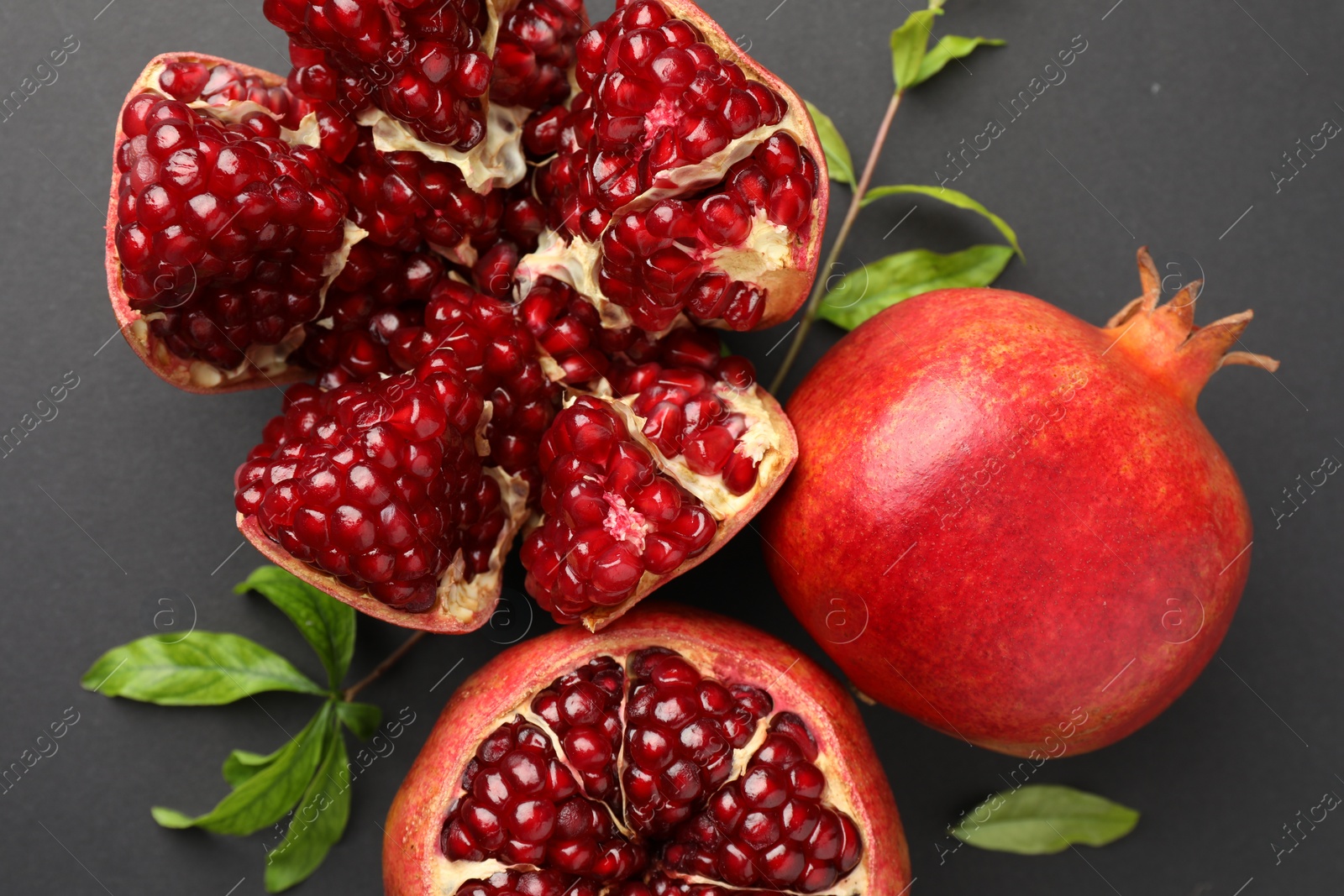 Photo of Fresh ripe pomegranates and leaves on grey background, top view