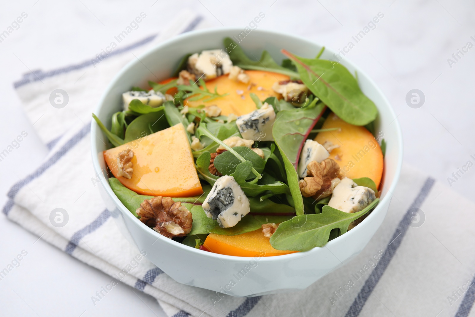 Photo of Tasty salad with persimmon, blue cheese and walnuts served on white table