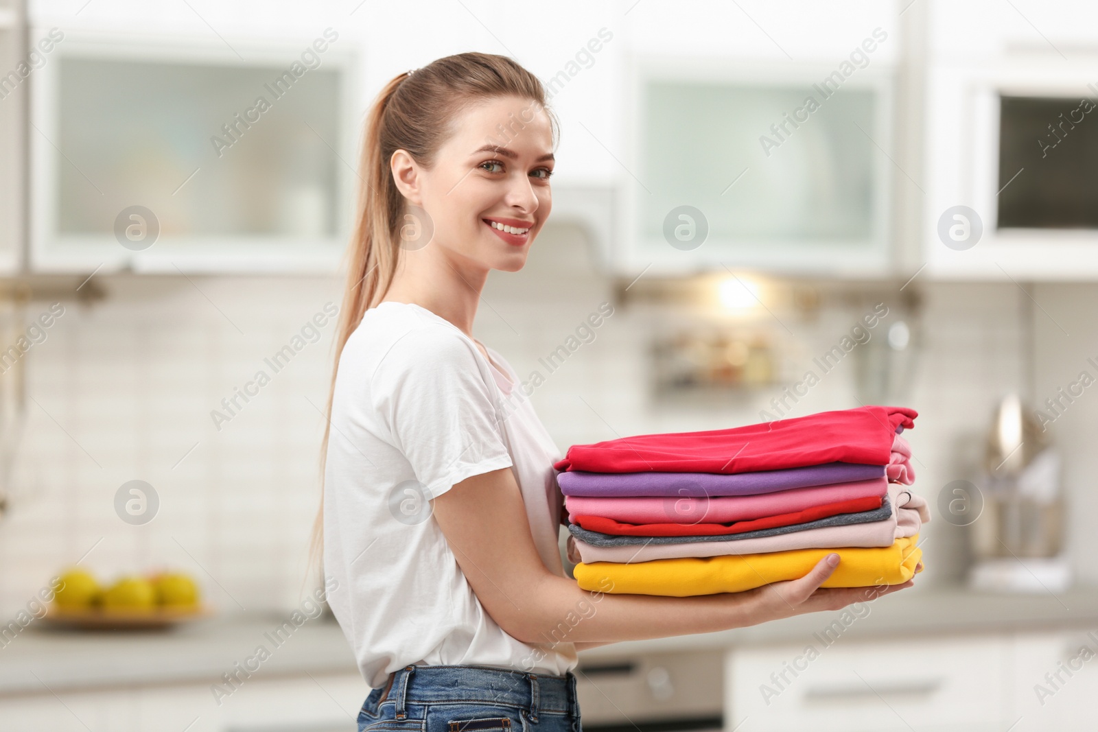 Photo of Woman holding folded clean clothes in kitchen. Laundry day