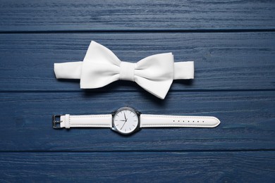 Stylish white bow tie and wristwatch on blue wooden table, flat lay