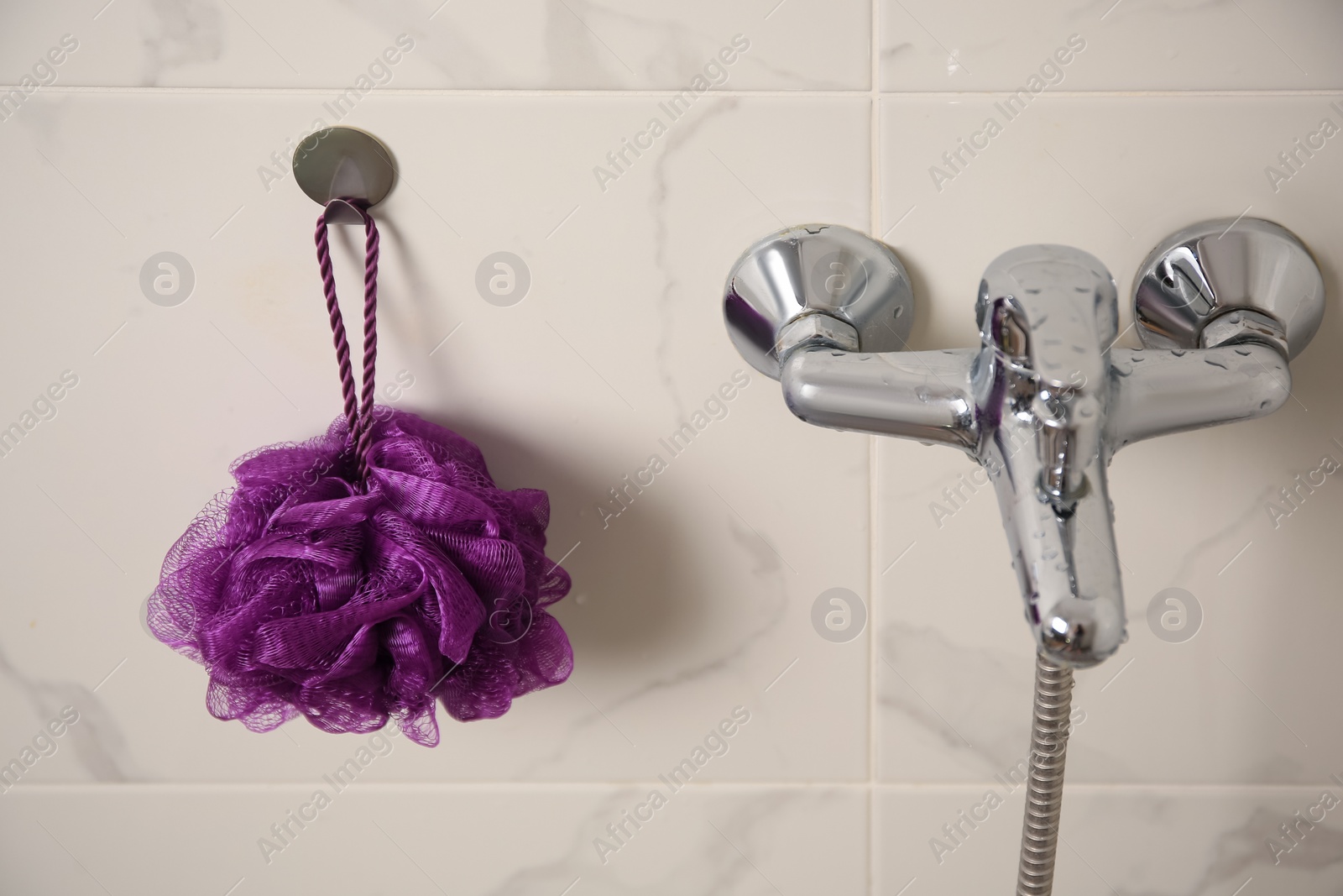 Photo of Purple shower puff hanging near faucet in bathroom