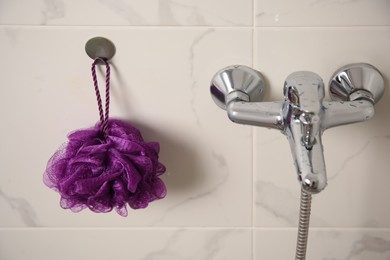 Purple shower puff hanging near faucet in bathroom