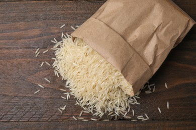 Photo of Overturned paper bag with raw rice on wooden table, top view