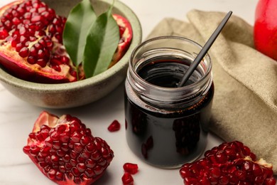 Photo of Glass jar of tasty pomegranate sauce and fresh ripe fruit on white marble table