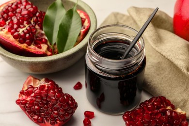 Glass jar of tasty pomegranate sauce and fresh ripe fruit on white marble table