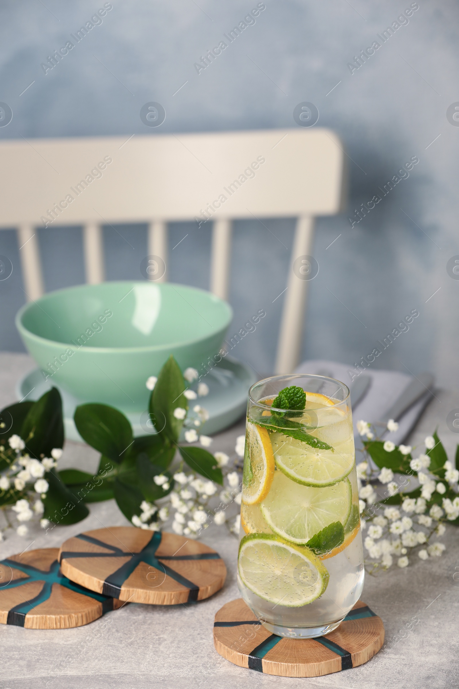 Photo of Glass of lemonade and stylish wooden cup coasters on light table