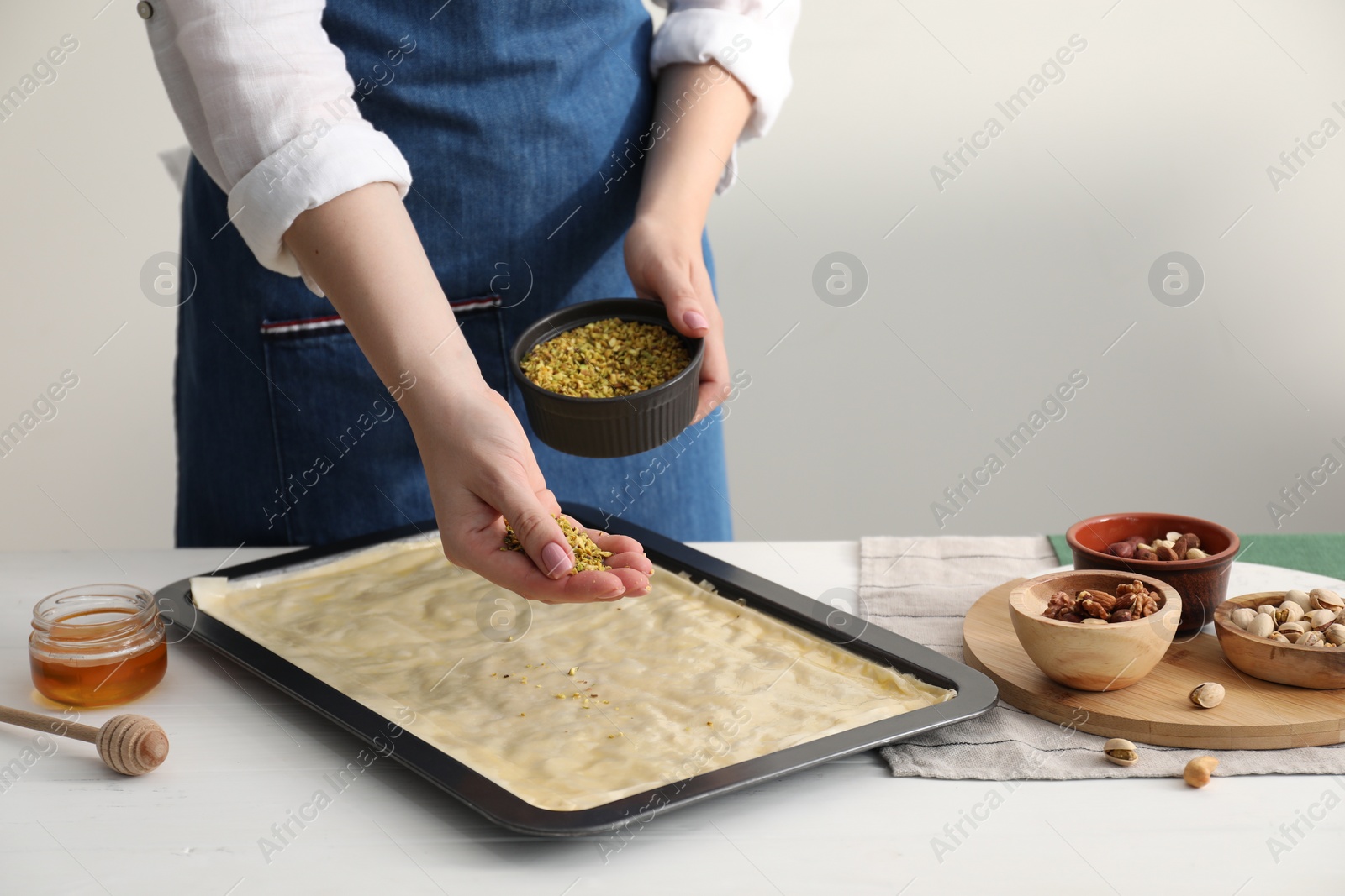 Photo of Making delicious baklava. Woman adding chopped nuts to dough at white wooden table, closeup. Space for text