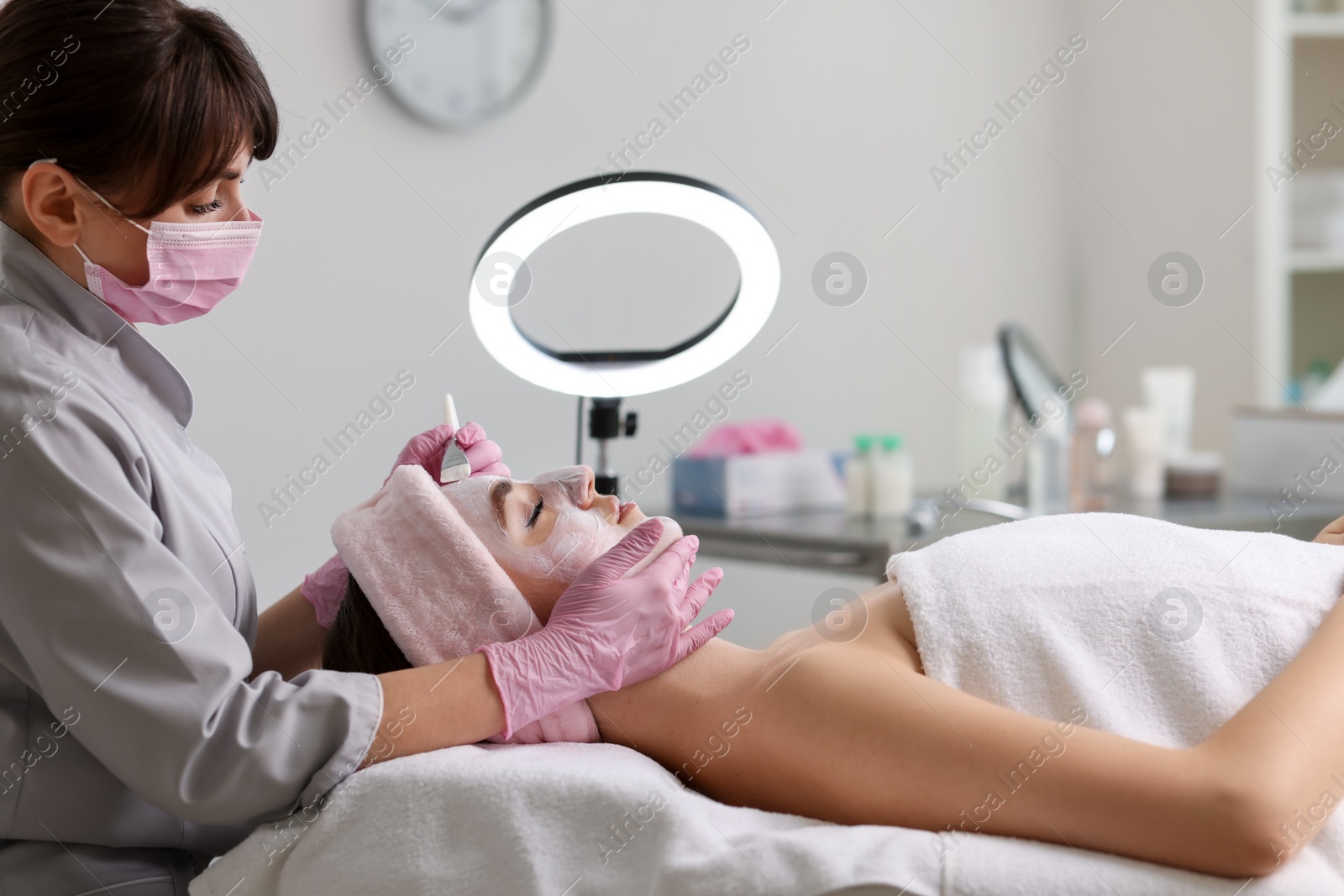 Photo of Cosmetologist applying mask on woman's face in clinic