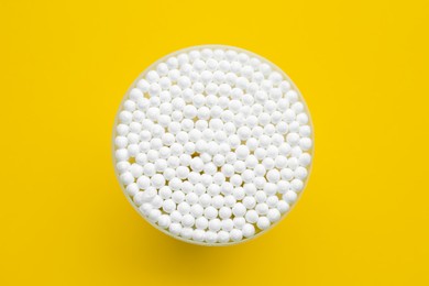 Photo of Many cotton buds in container on yellow background, top view