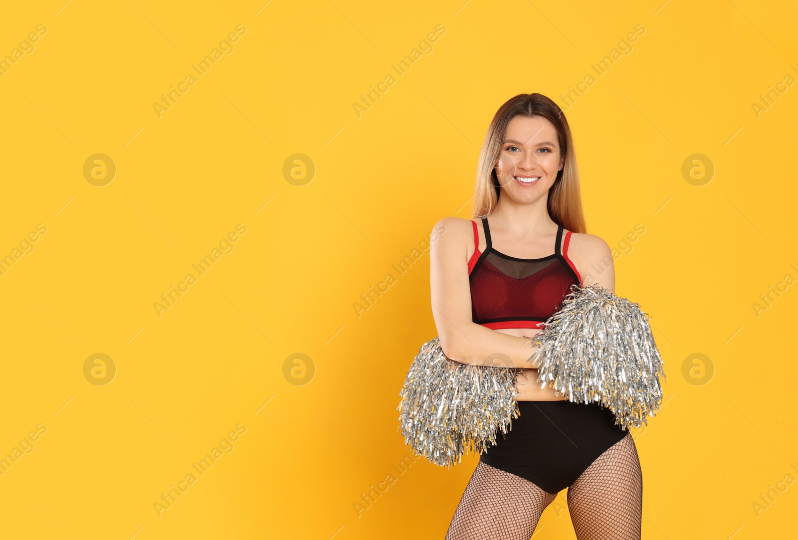 Photo of Beautiful cheerleader in costume holding pom poms on yellow background. Space for text