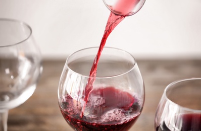 Pouring delicious red wine into glass on table, closeup