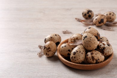 Photo of Fresh quail eggs and feathers on white wooden table. Space for text