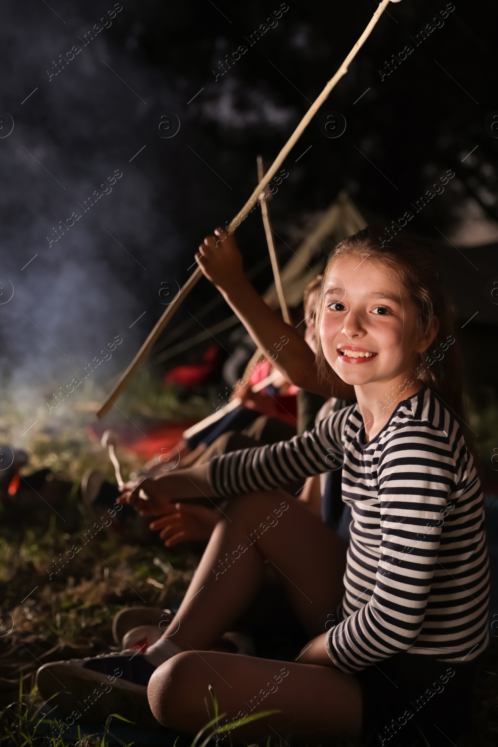 Photo of Adorable little girl near bonfire at night. Summer camp